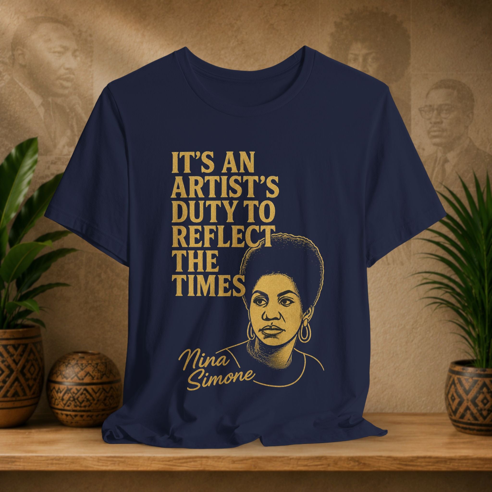 Navy blue t-shirt with gold text and Nina Simone's portrait on a wooden surface with plants and a textured wall in the background.