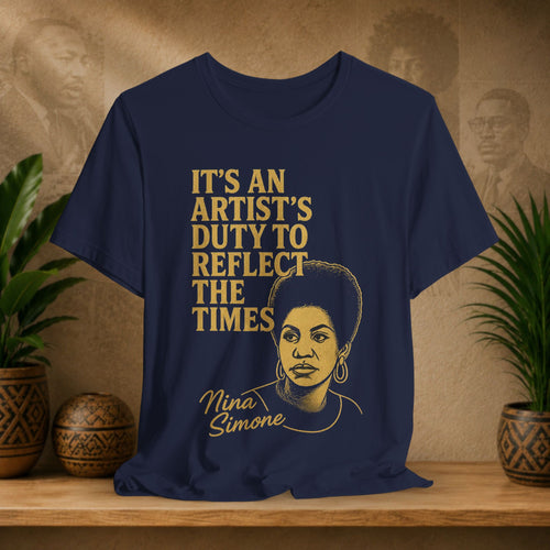 Navy blue t-shirt with gold text and Nina Simone's portrait on a wooden surface with plants and a textured wall in the background.