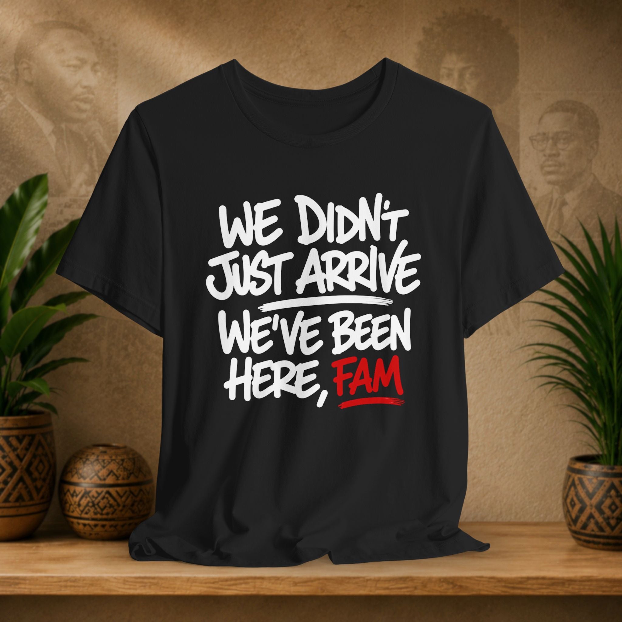 Black t-shirt with white and red text on a wooden surface with plants and a textured wall in the background