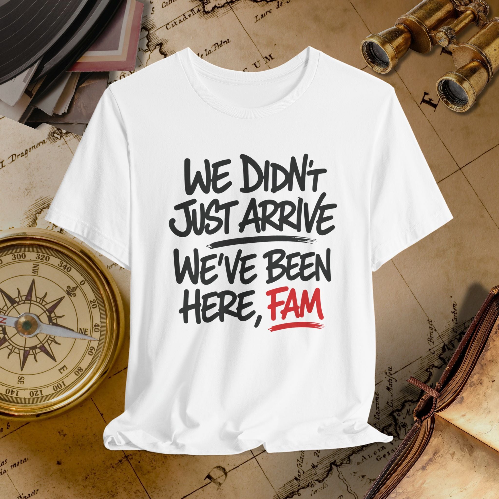 White t-shirt with text 'WE DIDN'T JUST ARRIVE WE'VE BEEN HERE, FAM' on a vintage map background.
