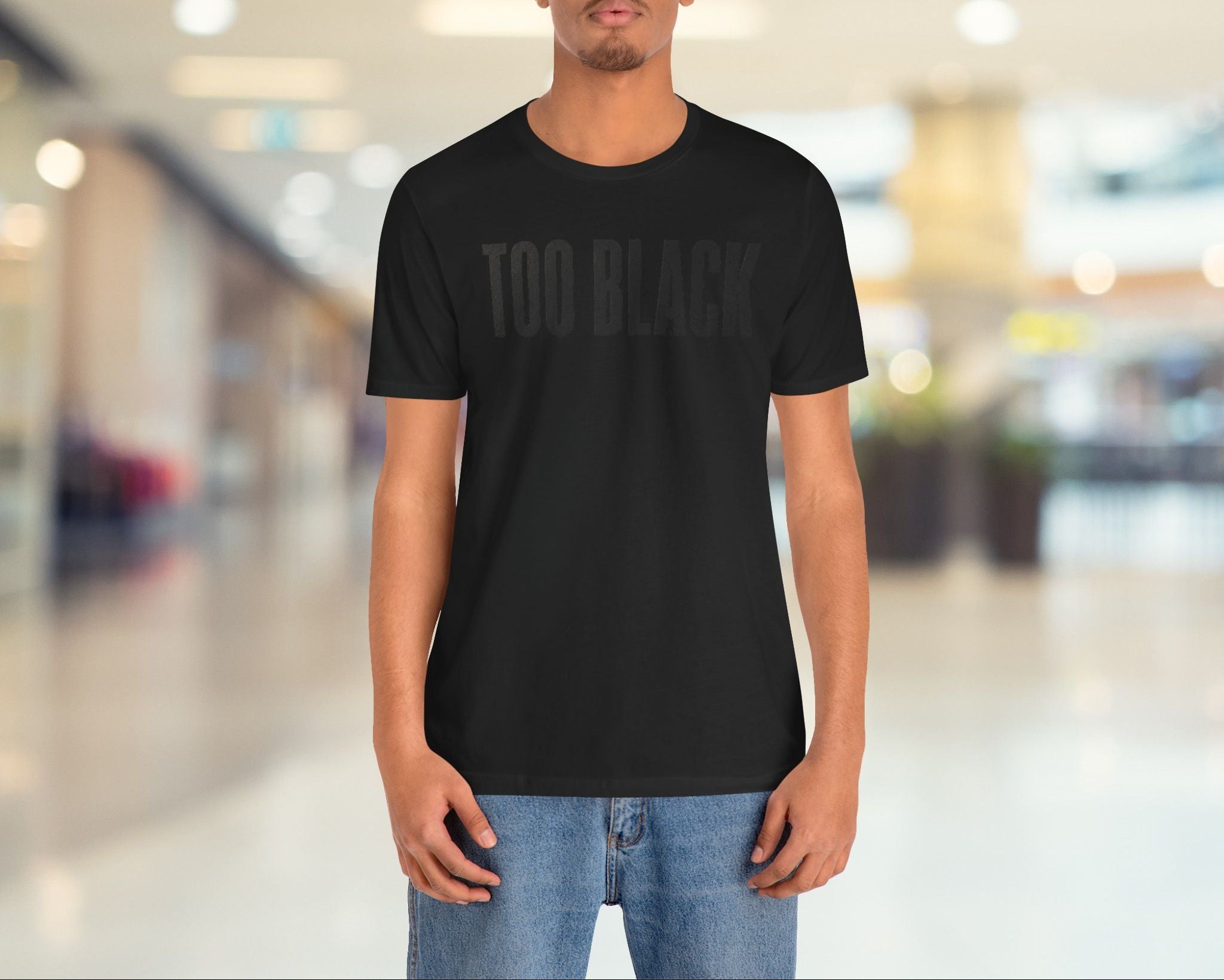 Person wearing a black t-shirt with 'TOO BLACK' text in a blurred indoor setting