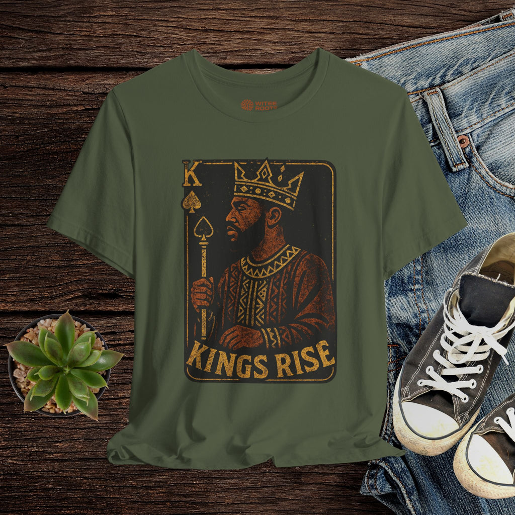 Green t-shirt with 'Kings Rise' graphic design on a wooden surface with jeans and sneakers.