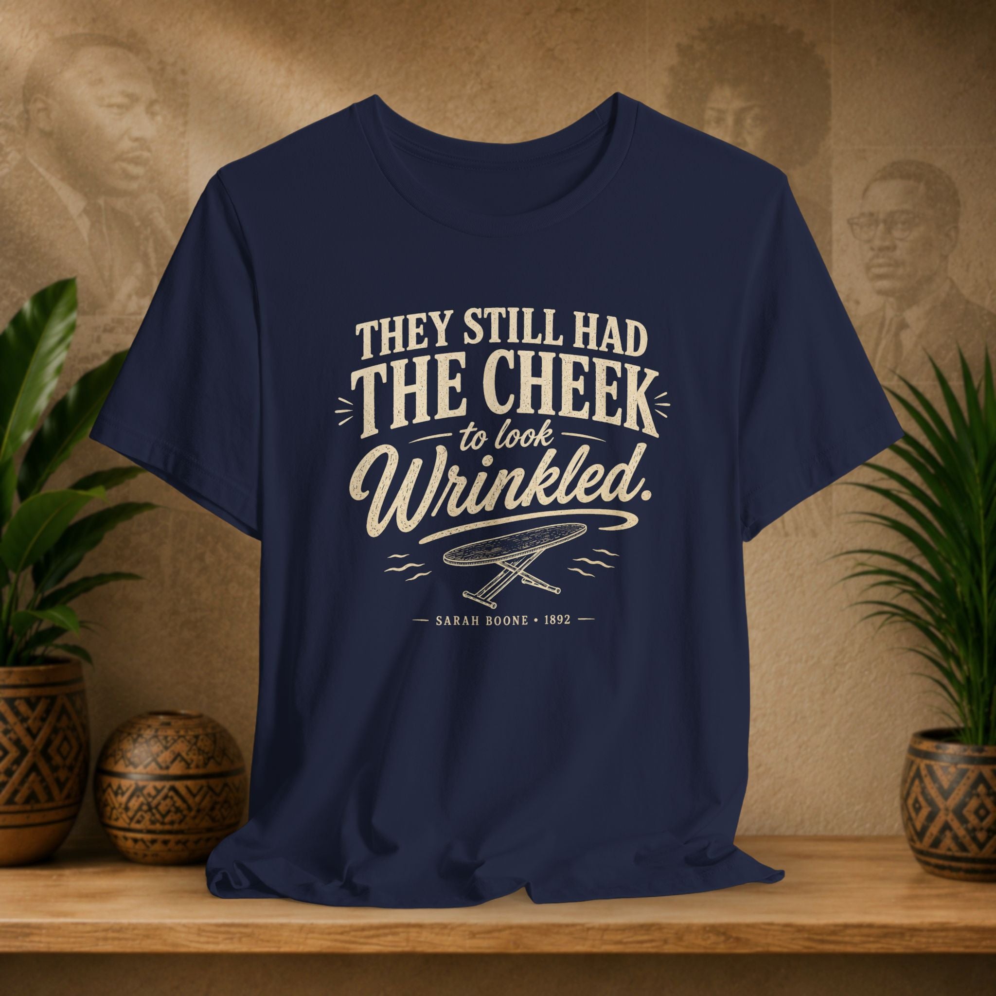 Navy blue t-shirt with white text on a wooden surface with plants and a vintage-style portrait in the background.