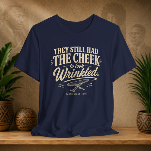 Navy blue t-shirt with white text on a wooden surface with plants and a vintage-style portrait in the background.