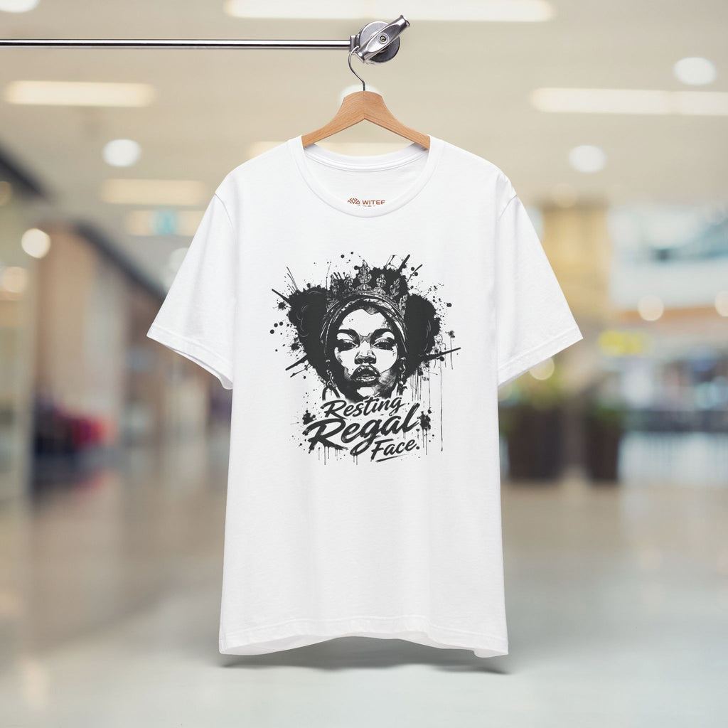 White t-shirt with black graphic design of a woman's face and text, hanging on a blurred indoor background.