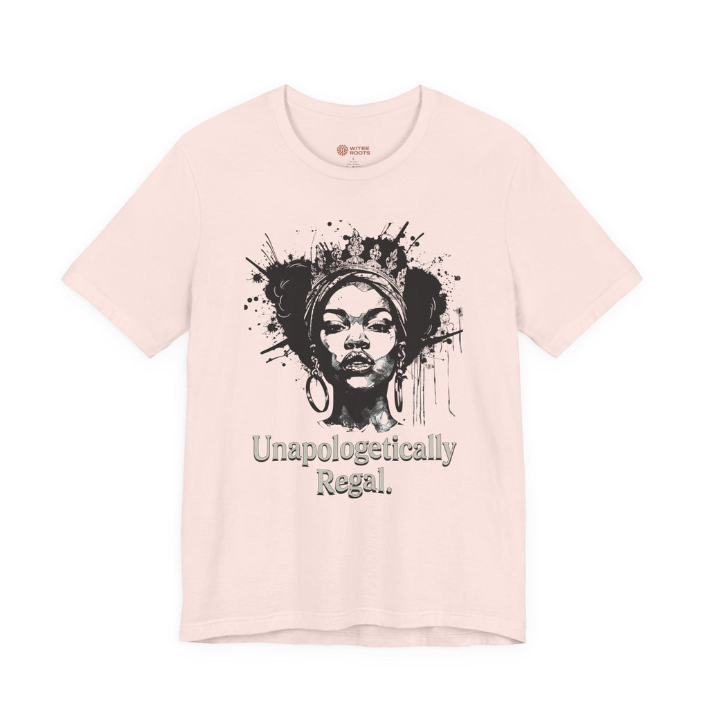 A light pink short-sleeve t-shirt with a black graphic of a woman's face surrounded by paint splatters and the text 'Unapologetically Regal.' printed below it.