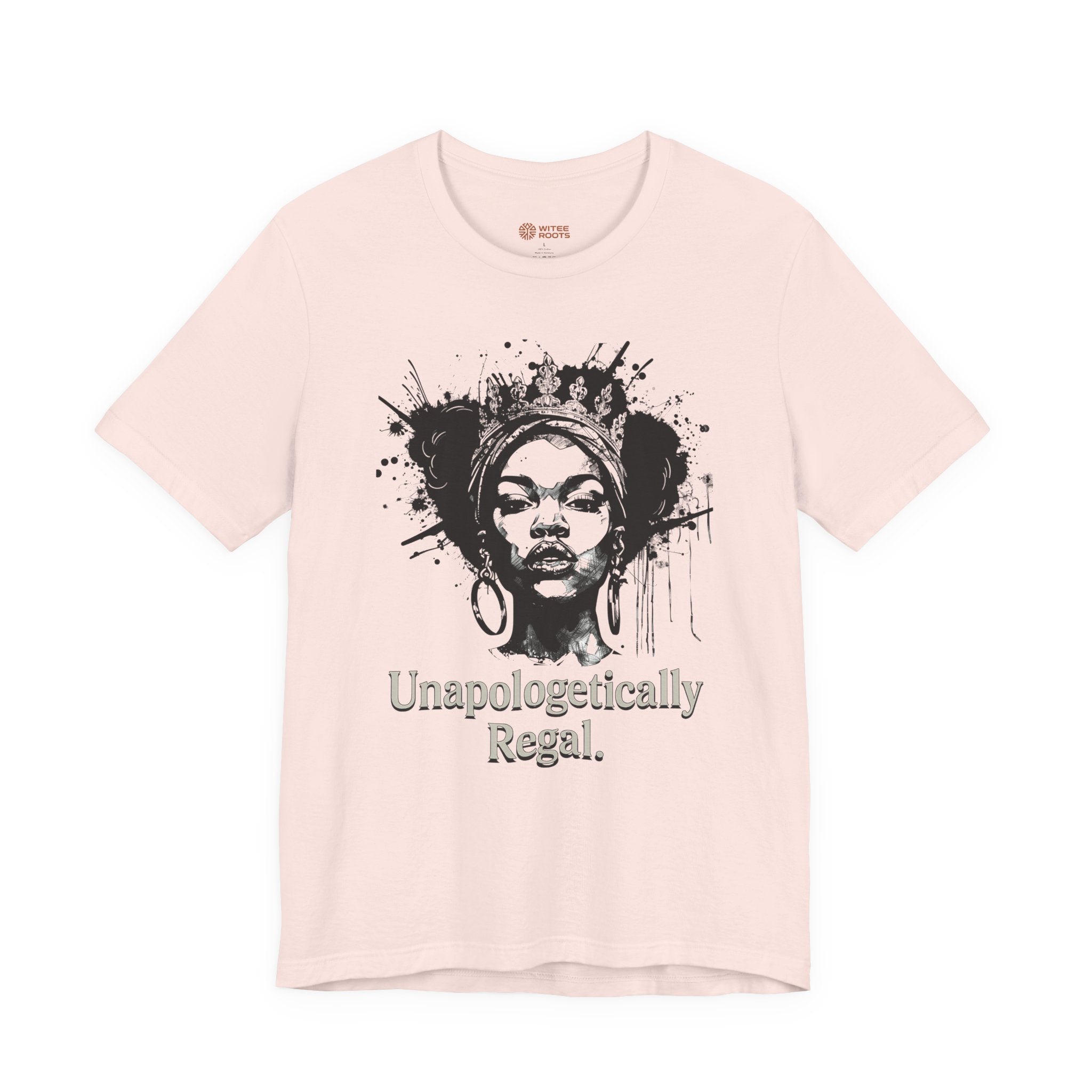 A light pink short-sleeve t-shirt with a black graphic of a woman's face surrounded by paint splatters and the text 'Unapologetically Regal.' printed below it.