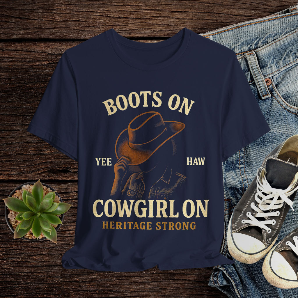 Navy blue t-shirt with cowboy graphic and text on a wooden surface with jeans and sneakers.
