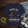 Navy blue t-shirt with cowboy graphic and text on a wooden surface with jeans and sneakers.