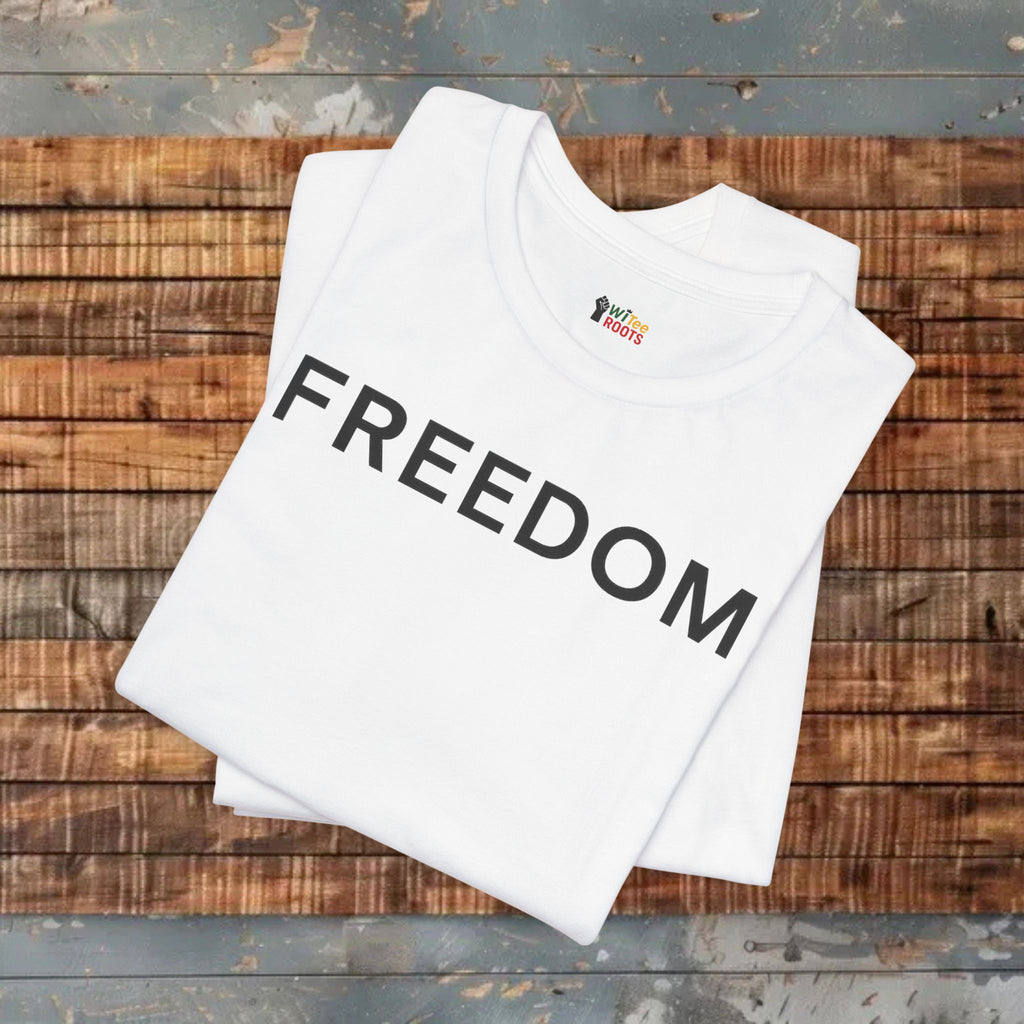 White t-shirt with 'FREEDOM' printed on it, folded on a wooden surface