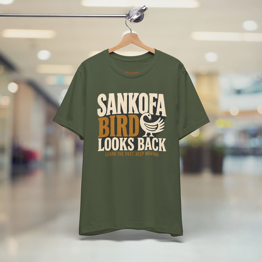 Green t-shirt with 'Sankofa Bird Looks Back' text on a hanger in a store.