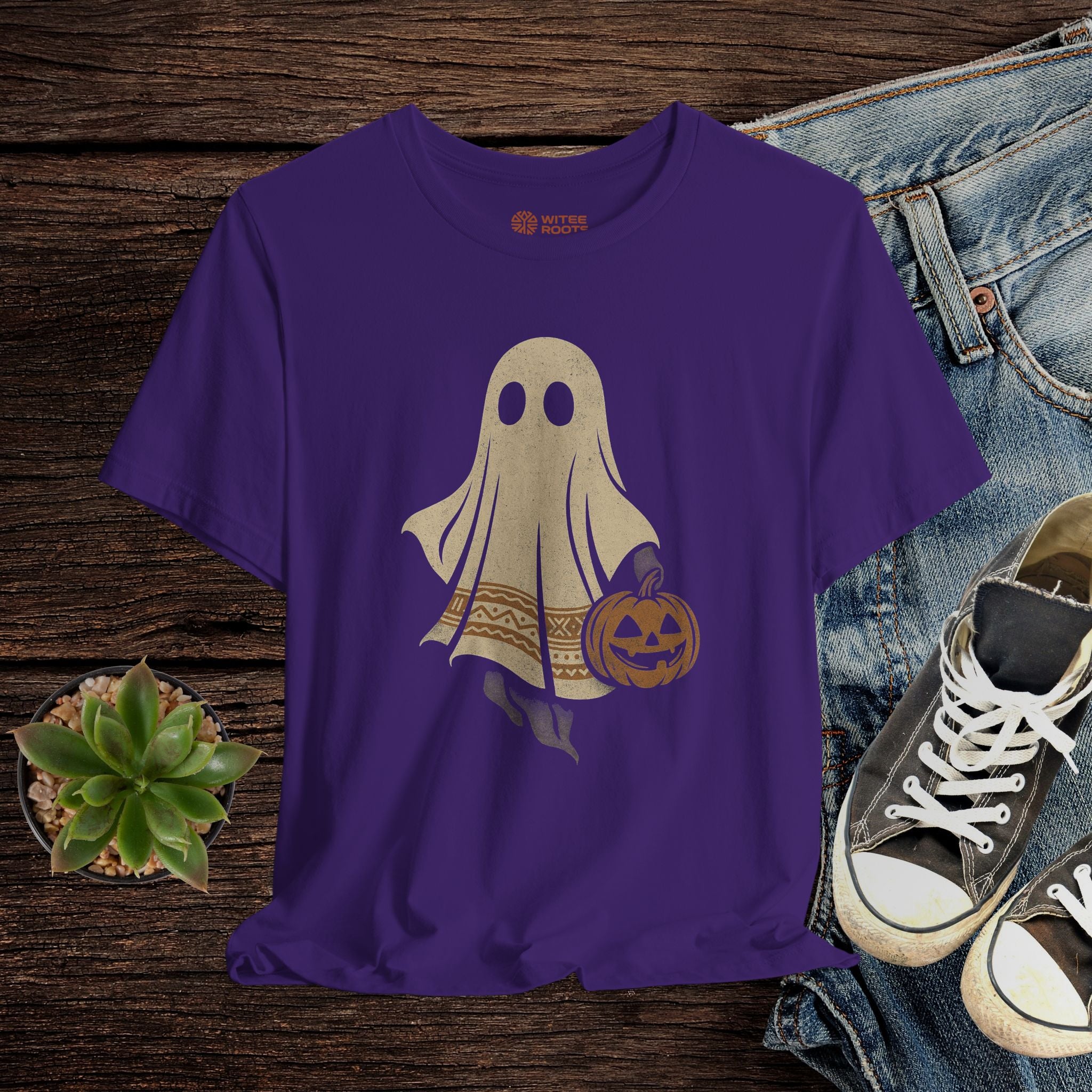 Purple t-shirt with ghost design on a wooden surface with jeans and sneakers.