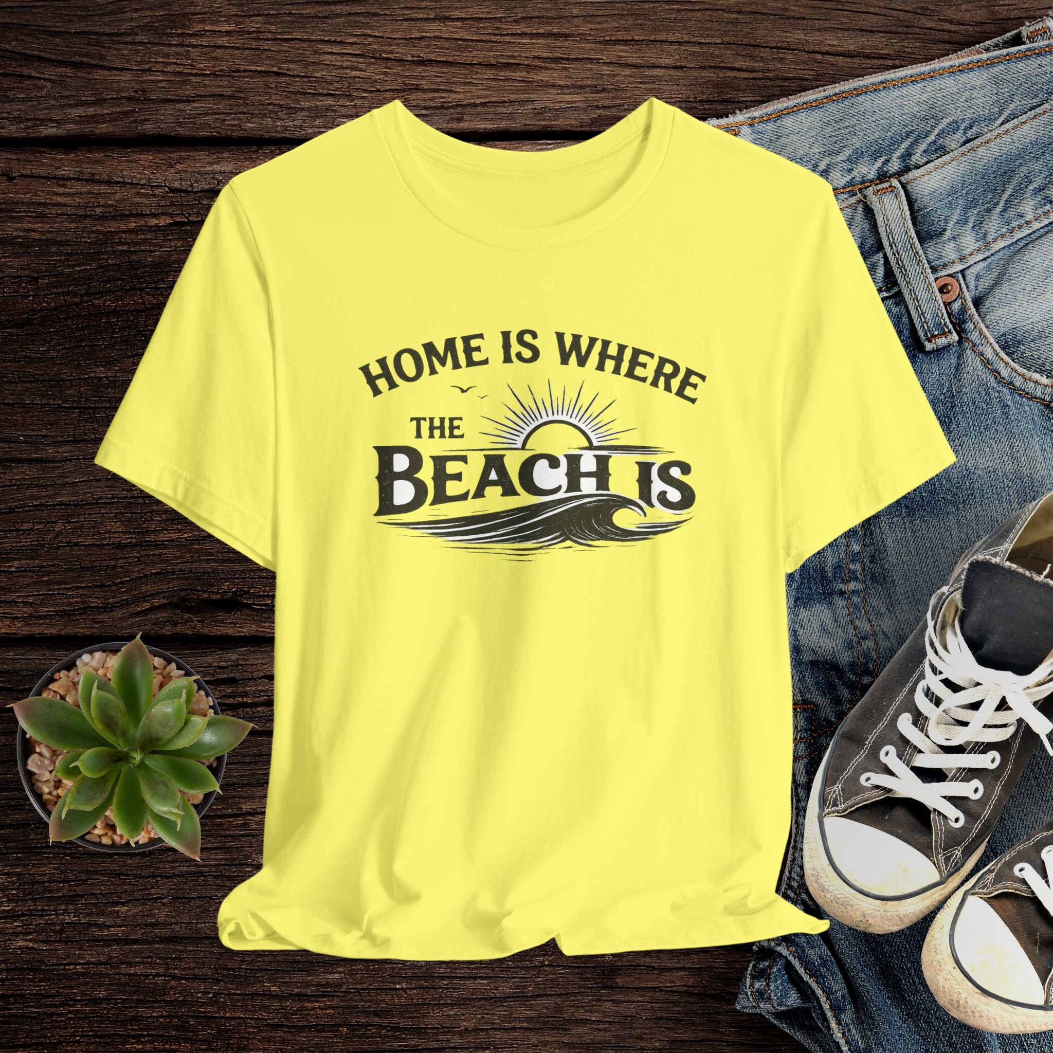 Yellow t-shirt with 'Home is where the beach is' text on a wooden surface with jeans and sneakers.