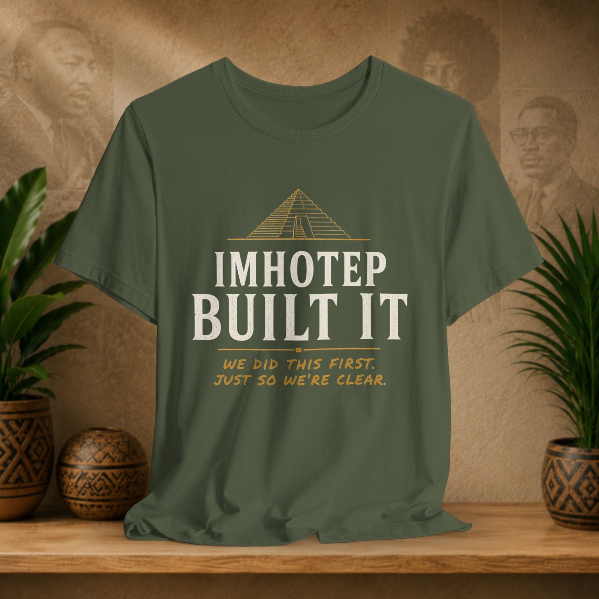 Green t-shirt with 'IMHOTEP BUILT IT' text on a wooden surface with plants and decorative items.