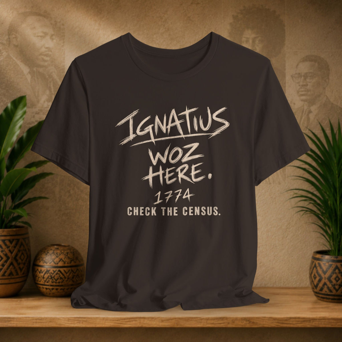 A brown graphic t-shirt displayed on a wooden shelf. The shirt features a distressed white print that reads 'Ignatius Woz Here.