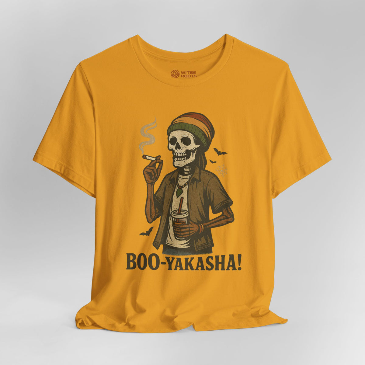 A mustard yellow t-shirt with a graphic of a skeleton wearing a Rasta hat and jacket, smoking a cigar and holding a cup, with the text 'BOO-YAKASHA!' printed below. The shirt is displayed on a neutral light gray background.