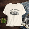 Beige t-shirt with 'Home is where the beach is' text on a wooden surface with jeans and sneakers.