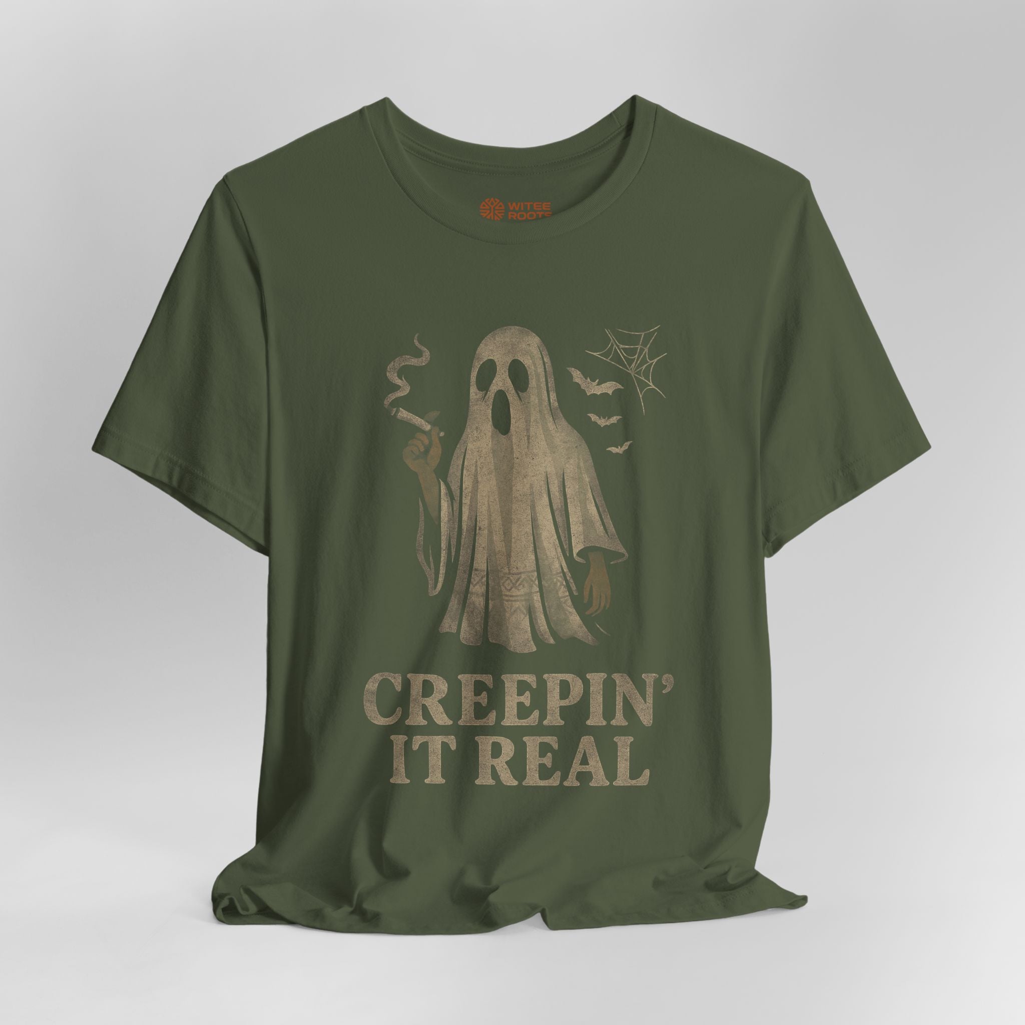 An olive green short-sleeve t-shirt with a distressed graphic of a ghost holding a cigarette, accompanied by the text 'CREEPIN' IT REAL' in a vintage font, displayed on a neutral gray background.