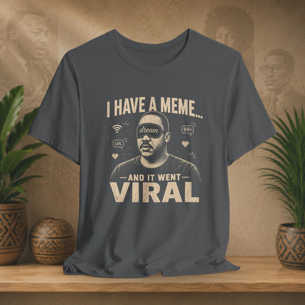 Gray t-shirt with graphic design and text on a wooden surface with plants and a textured wall background