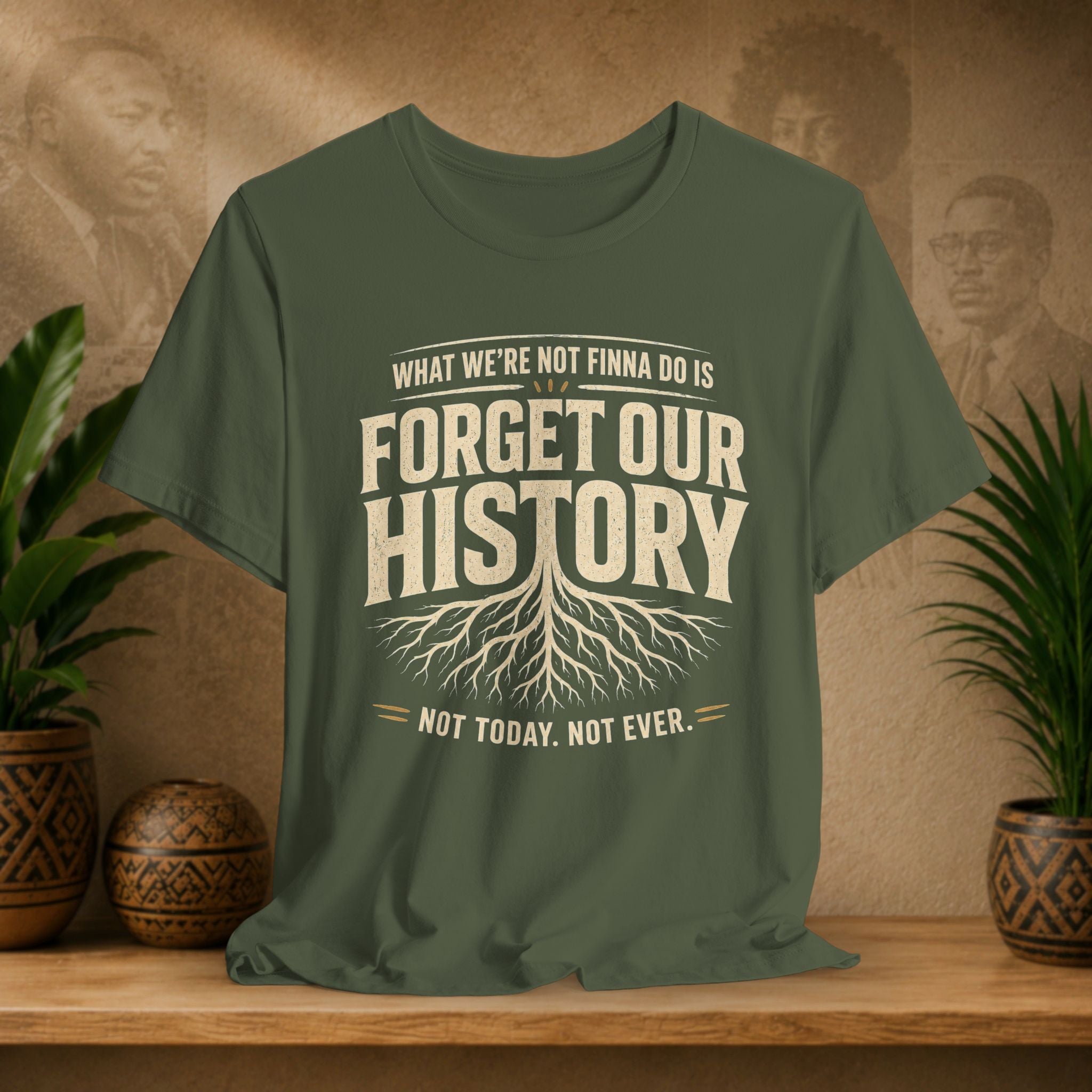Green t-shirt with 'Forget Our History' text on a wooden surface with plants and a textured wall background