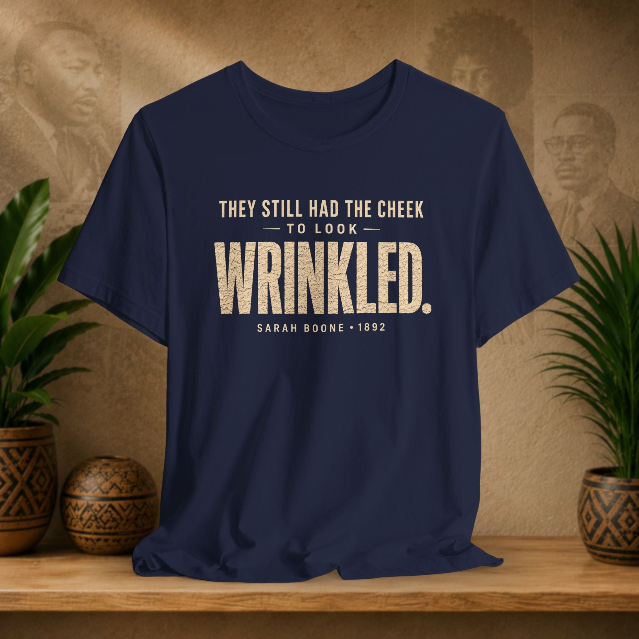 Navy blue t-shirt with white text on a wooden surface with plants and a textured wall background