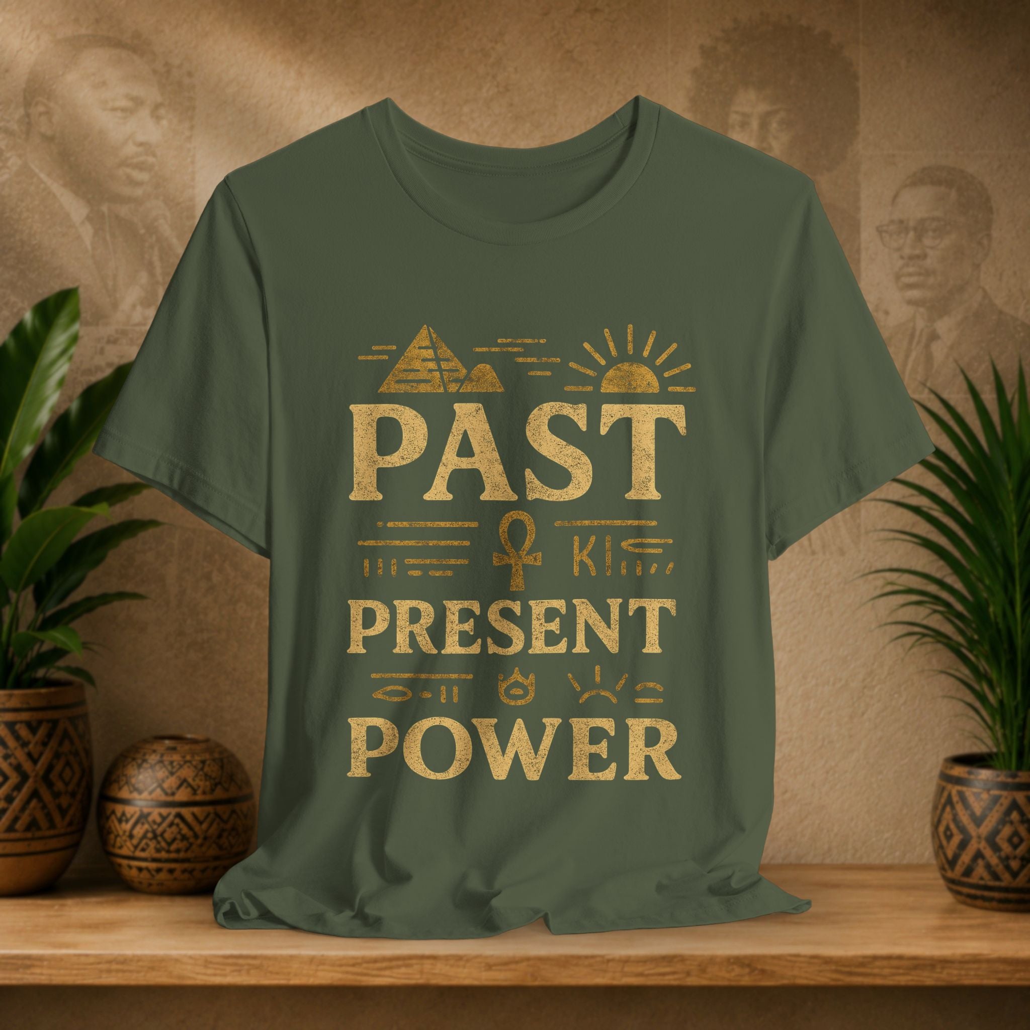 Green t-shirt with gold text on a wooden shelf with plants and decorative items.