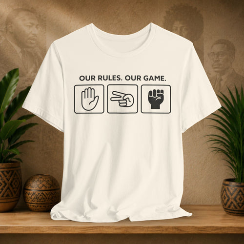 Beige t-shirt with text and symbols on a wooden surface with plants and a textured wall in the background.