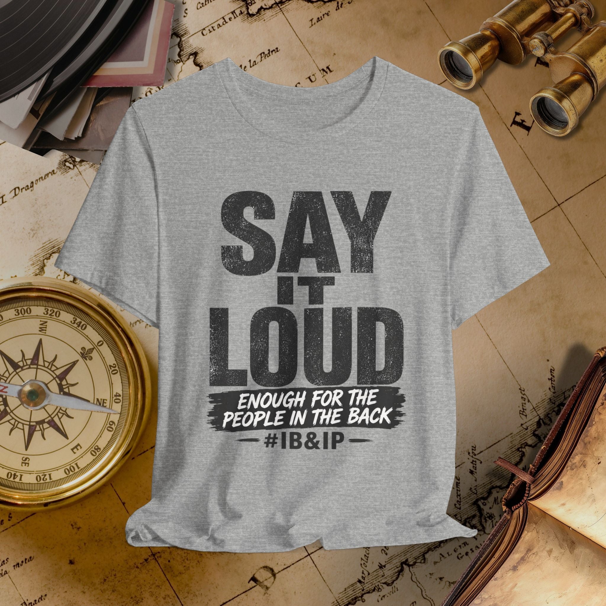 Gray t-shirt with text 'SAY IT LOUD ENOUGH FOR THE PEOPLE IN THE BACK #IB&IP' on a vintage map background.