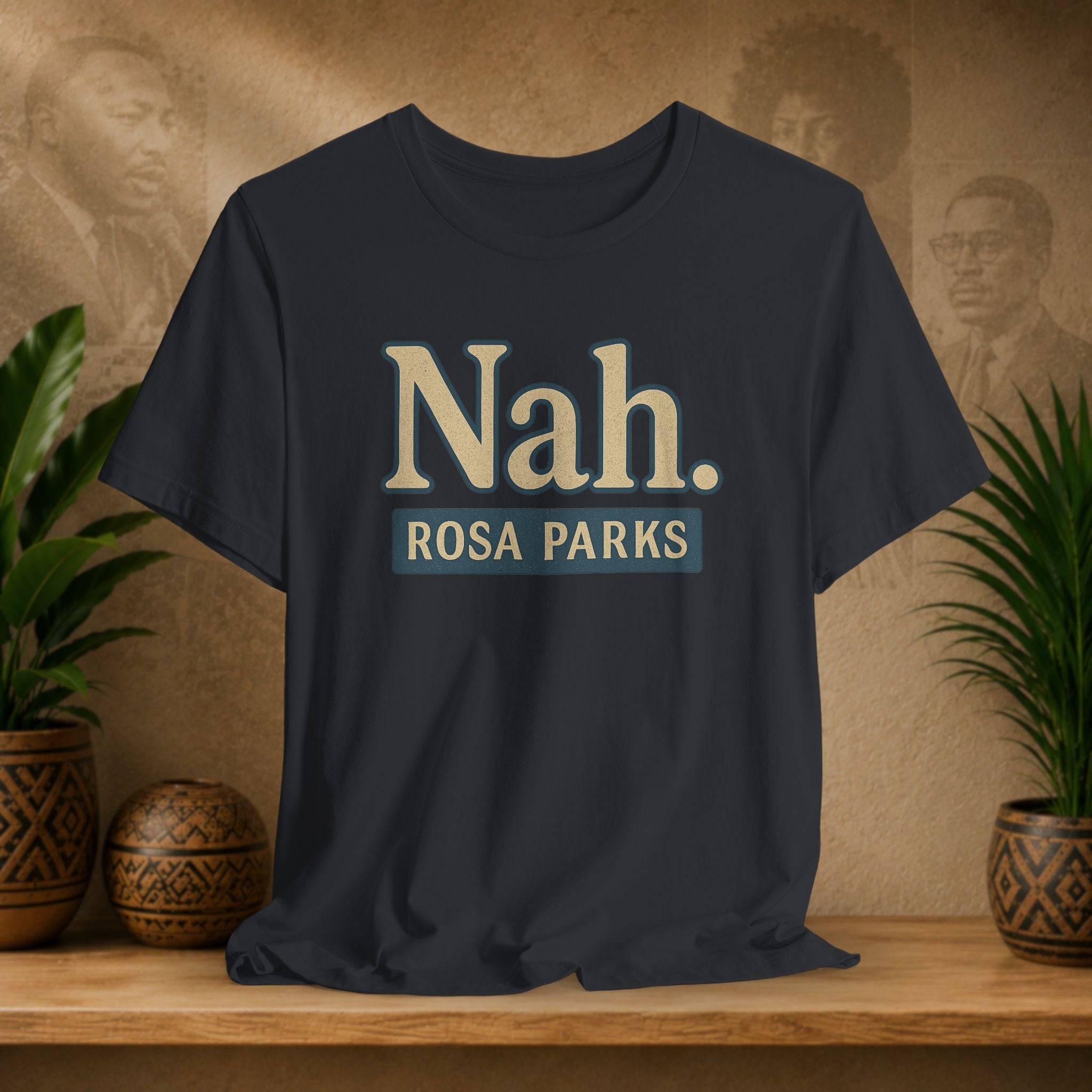 Black t-shirt with 'Nah. ROSA PARKS' text on a wooden surface with plants and a blurred background.