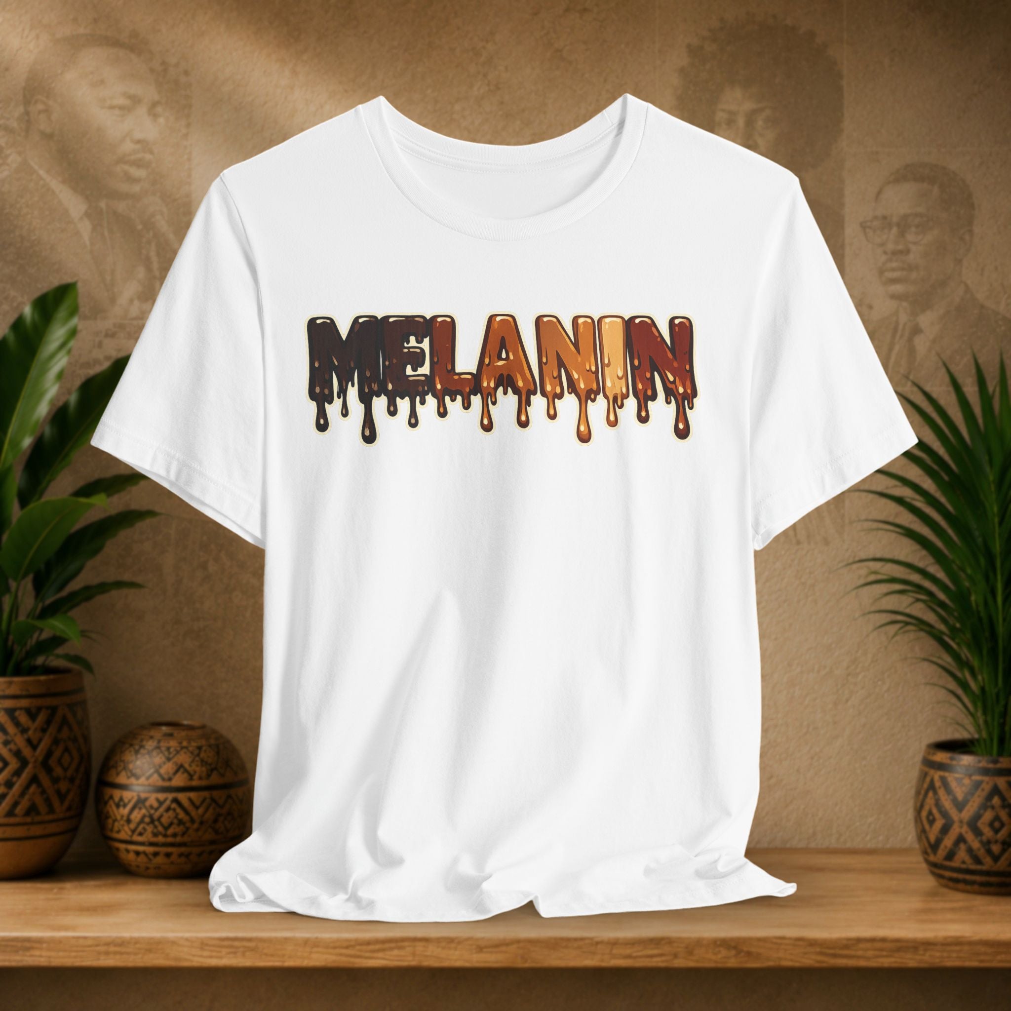 A white short-sleeve t-shirt with a 'MELANIN' text graphic in a dripping paint style, styled on a wooden shelf with potted plants against a textured brown background.