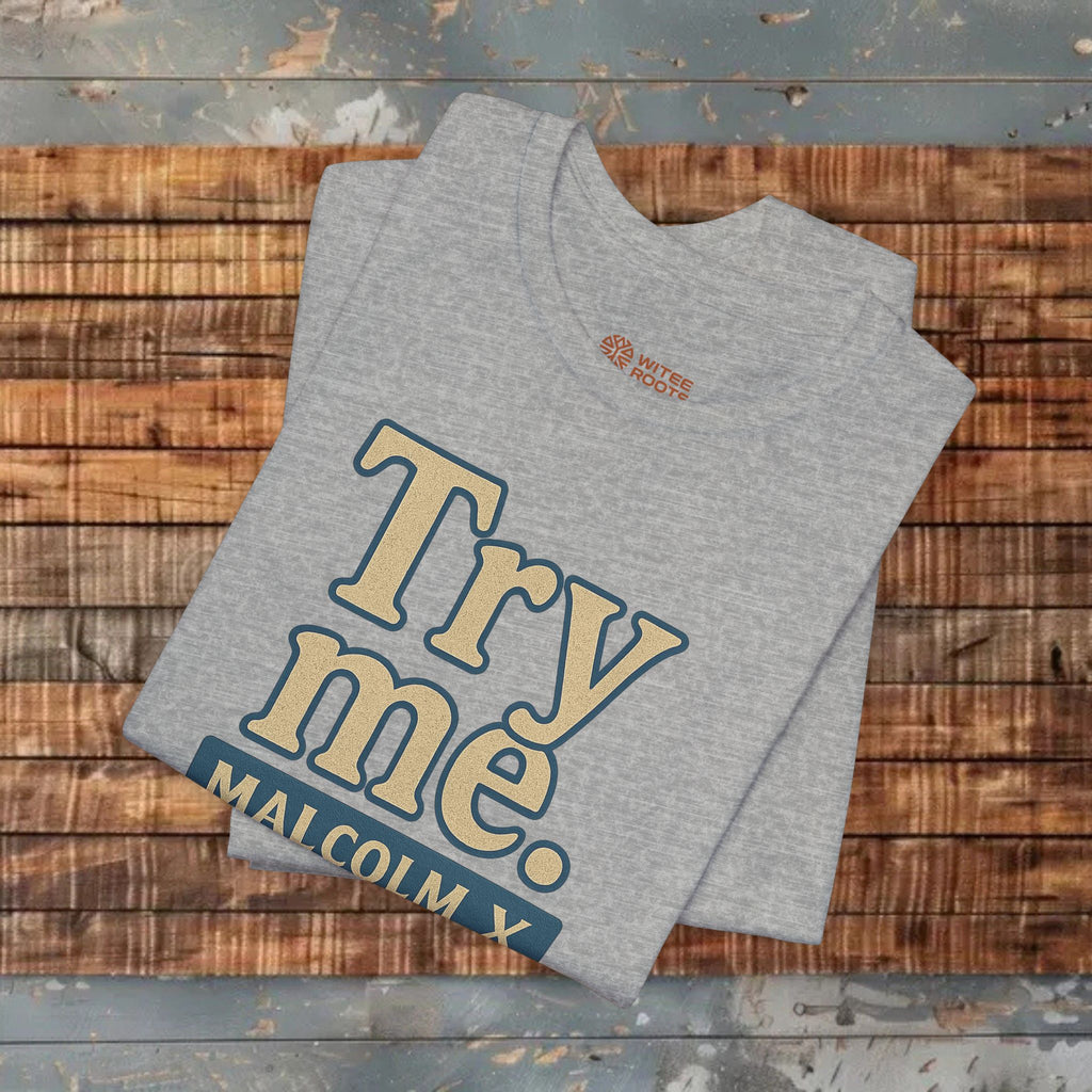 Gray t-shirt with 'Try me. MALCOLM X' text on a wooden surface