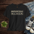 Black t-shirt with 'UNAPOLOGETICALLY BLACK' text on a wooden surface with jeans and sneakers.