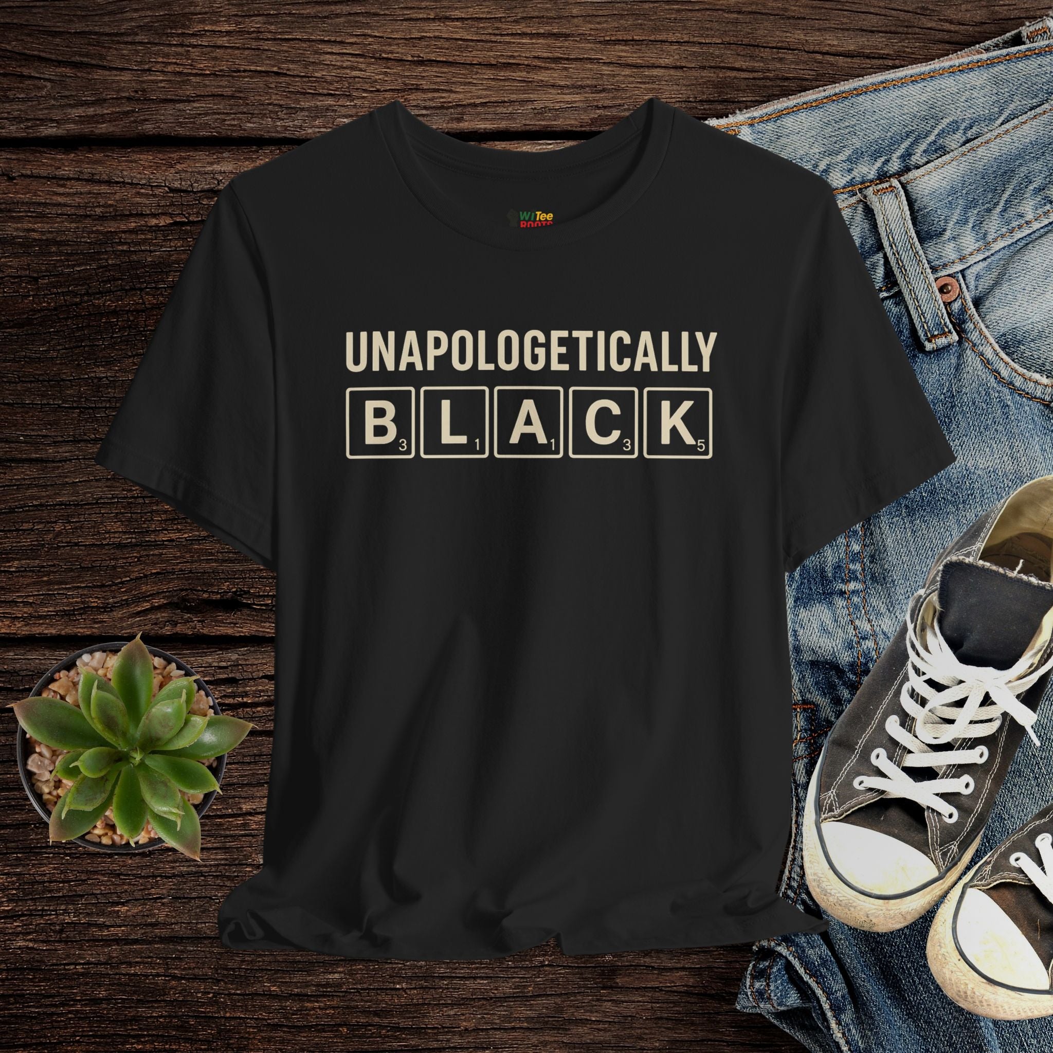 Black t-shirt with 'UNAPOLOGETICALLY BLACK' text on a wooden surface with jeans and sneakers.