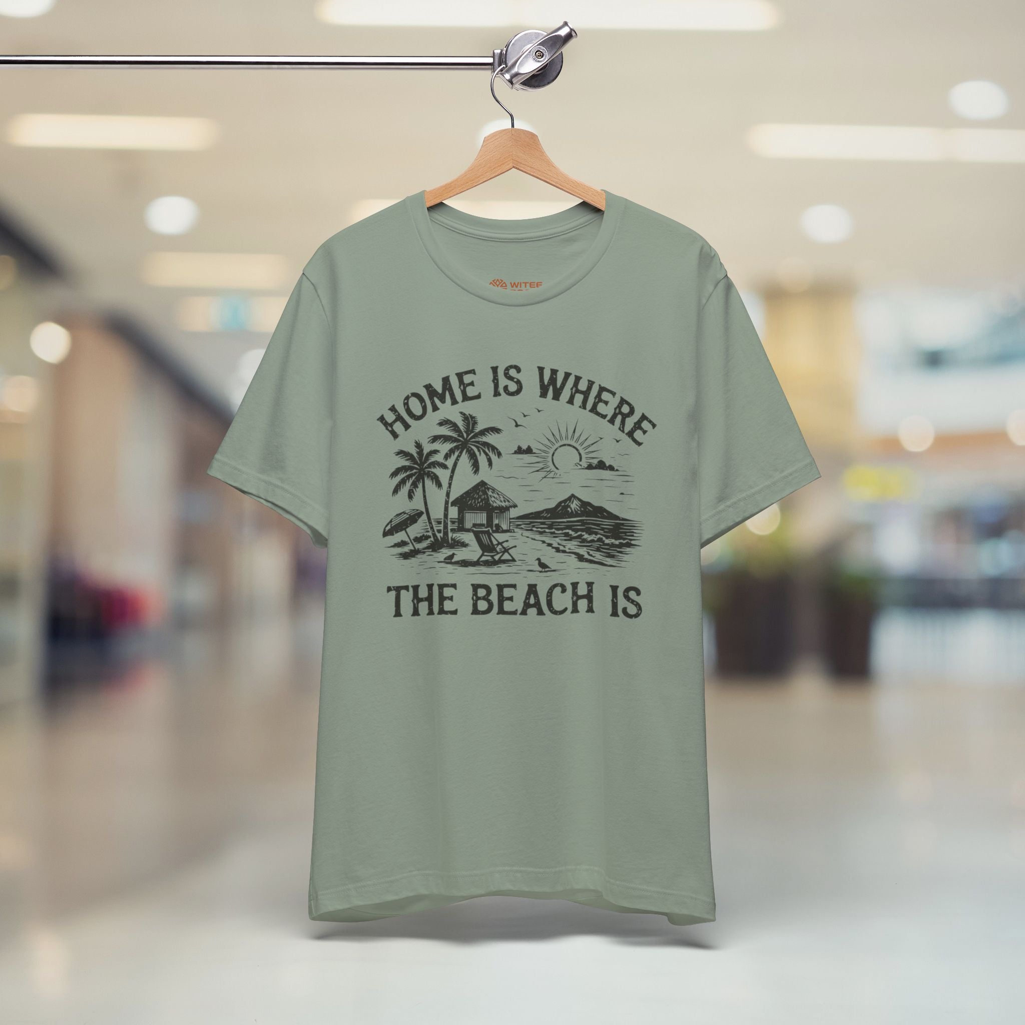 Green t-shirt with beach graphic and text on a hanger in a store.