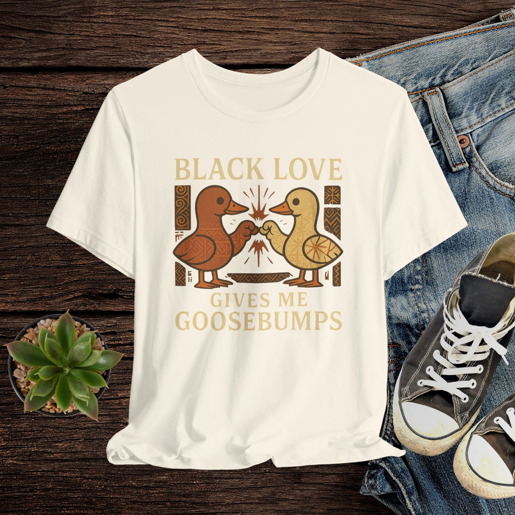 Beige t-shirt with 'Black Love Gives Me Goosebumps' graphic on a wooden surface with jeans and sneakers.