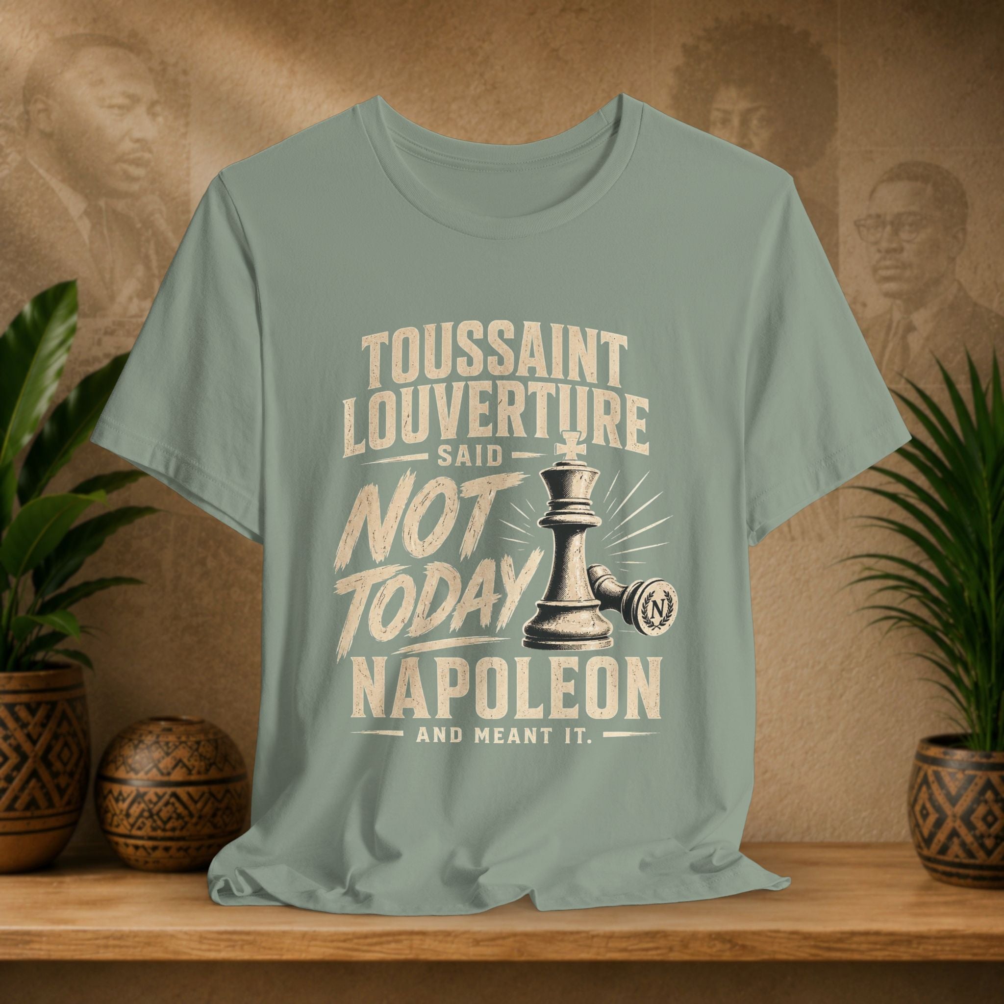 Green t-shirt with historical quote design on a wooden surface with plants and portraits in the background