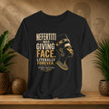 Black t-shirt with gold text and graphic of a historical figure on a wooden surface with plants and decorative items.