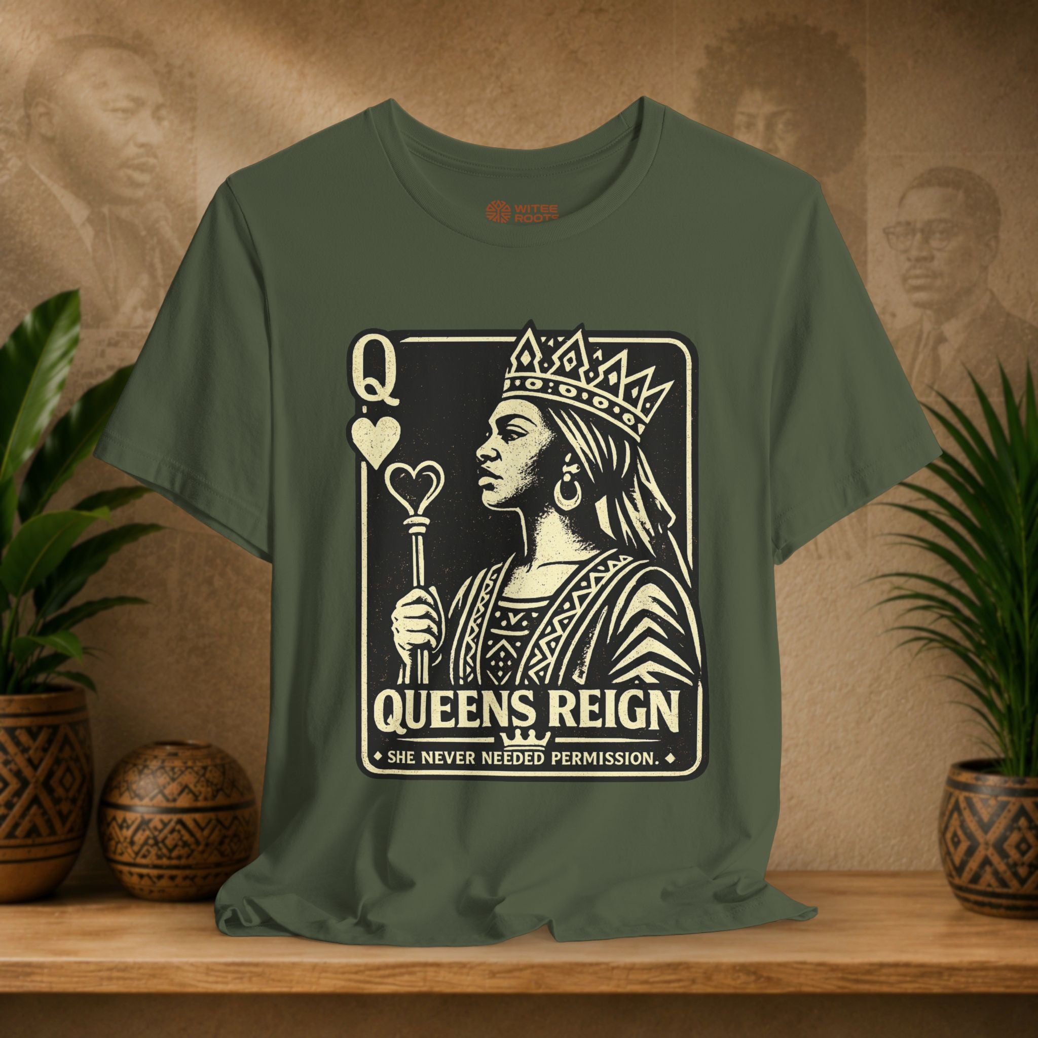 Green t-shirt with a graphic design of a queen and text on a wooden surface with plants and a textured wall in the background.