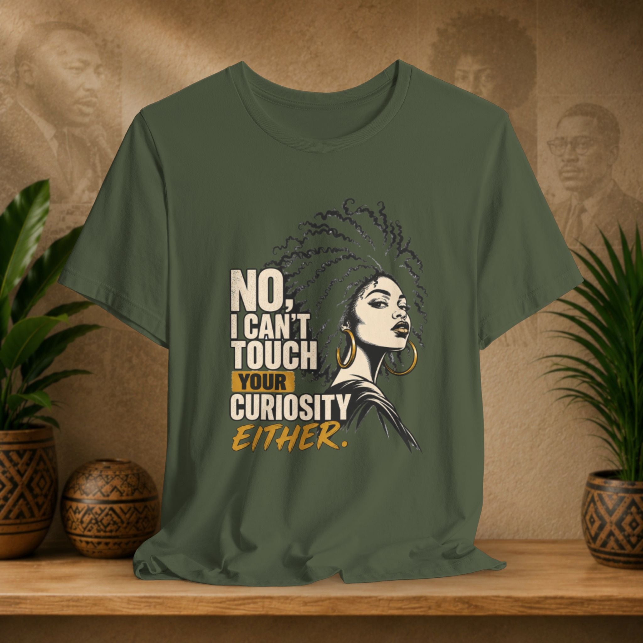 An olive green graphic t-shirt displayed on a wooden shelf. The shirt features a stylized illustration of a woman with an afro and gold hoop earrings next to the text 'NO, I CAN'T TOUCH YOUR CURIOSITY EITHER.