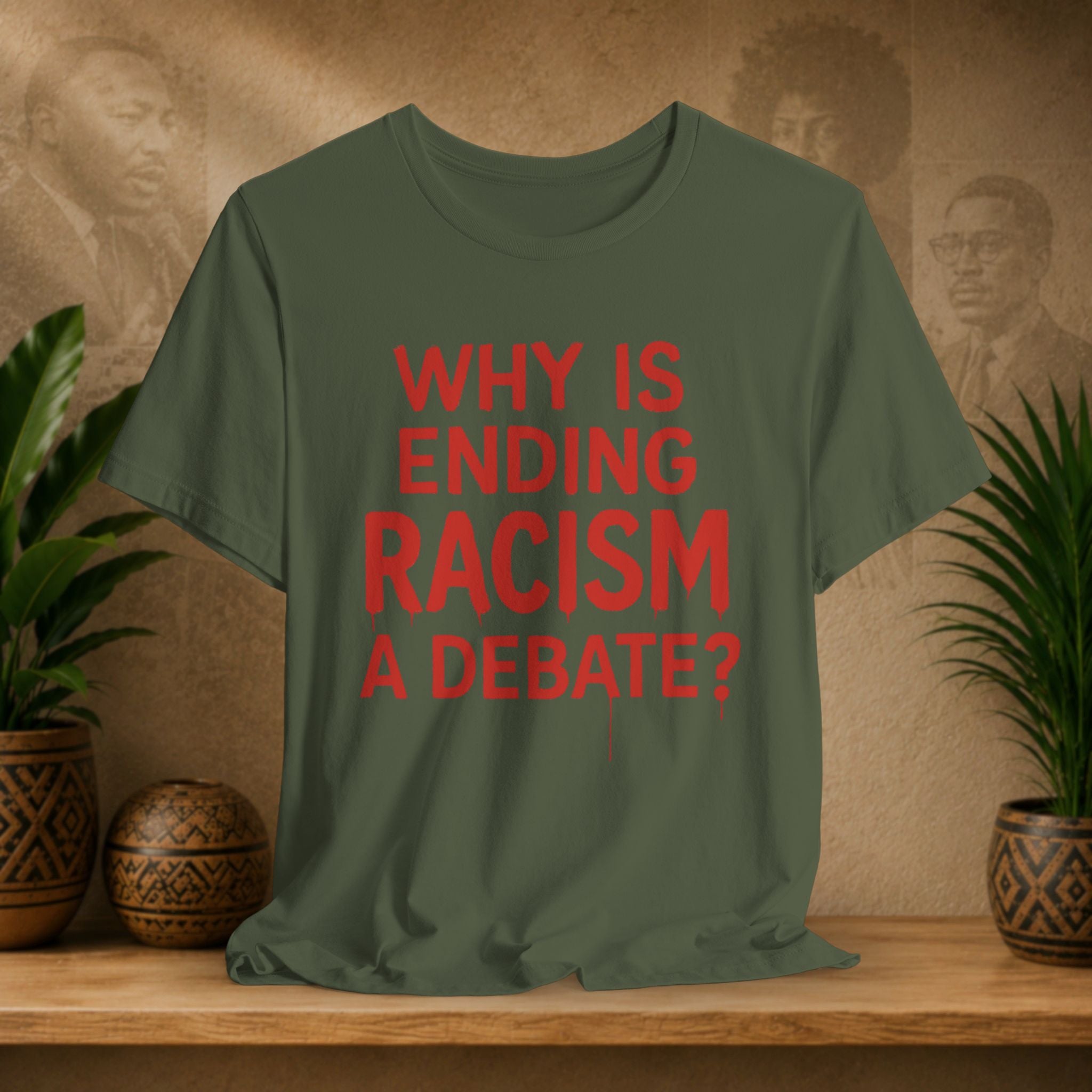 Green t-shirt with red text 'Why is ending racism a debate?' on a wooden surface with a decorative background.