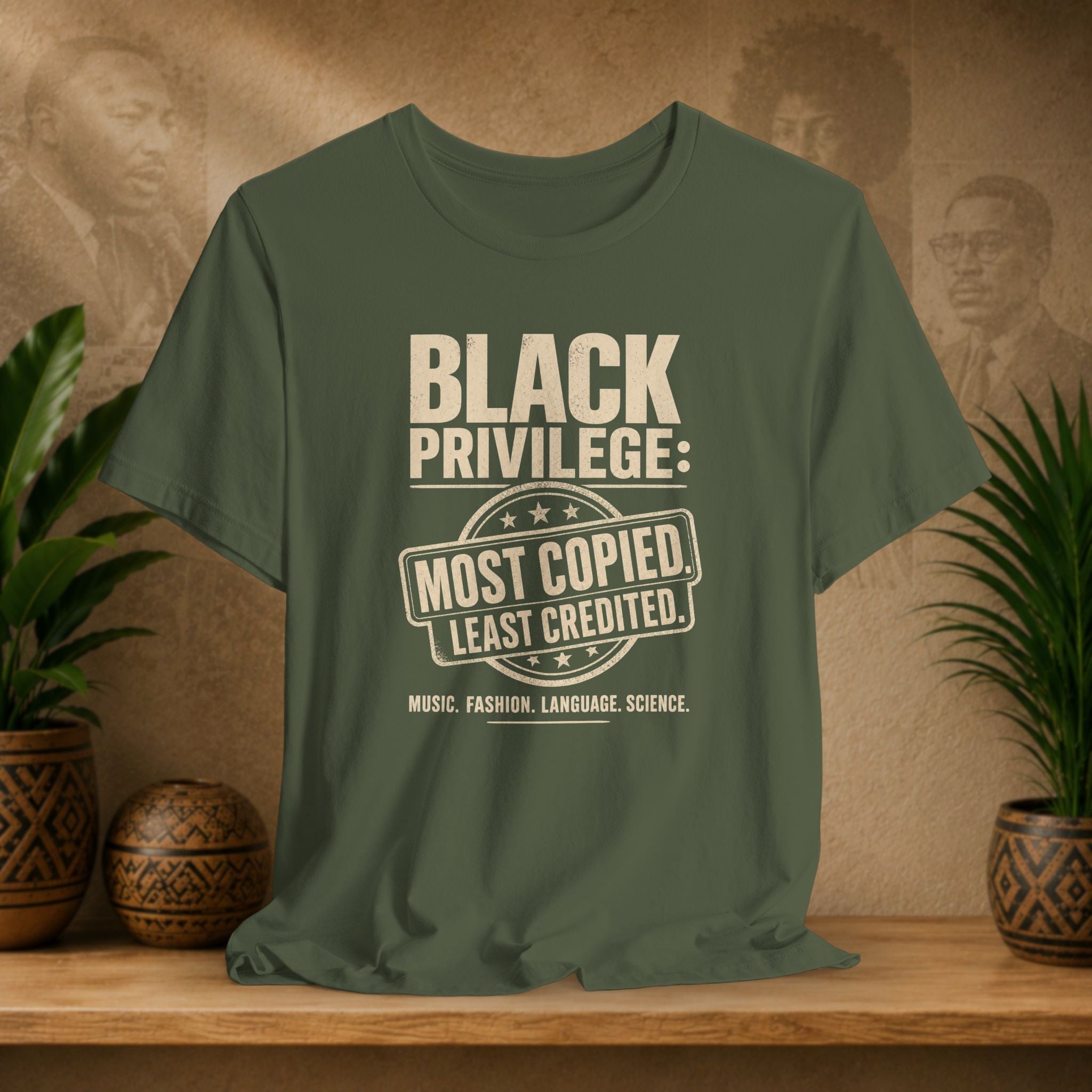 Green t-shirt with 'Black Privilege' text on a wooden surface with plants and a decorative wall in the background