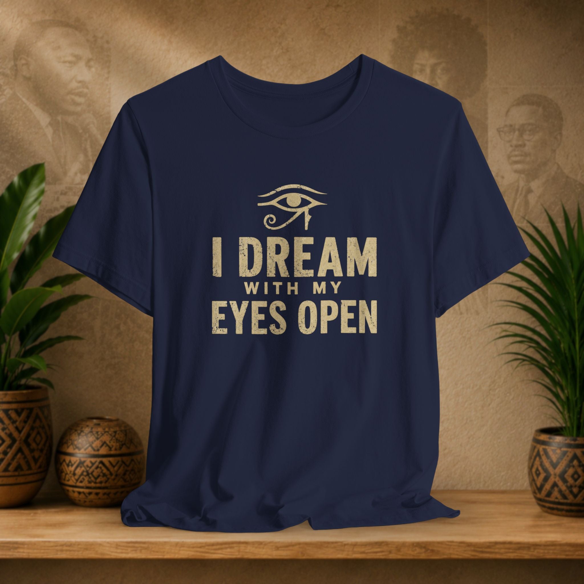 Navy blue t-shirt with 'I Dream with My Eyes Open' text and eye symbol on a wooden surface with plants and decorative items.