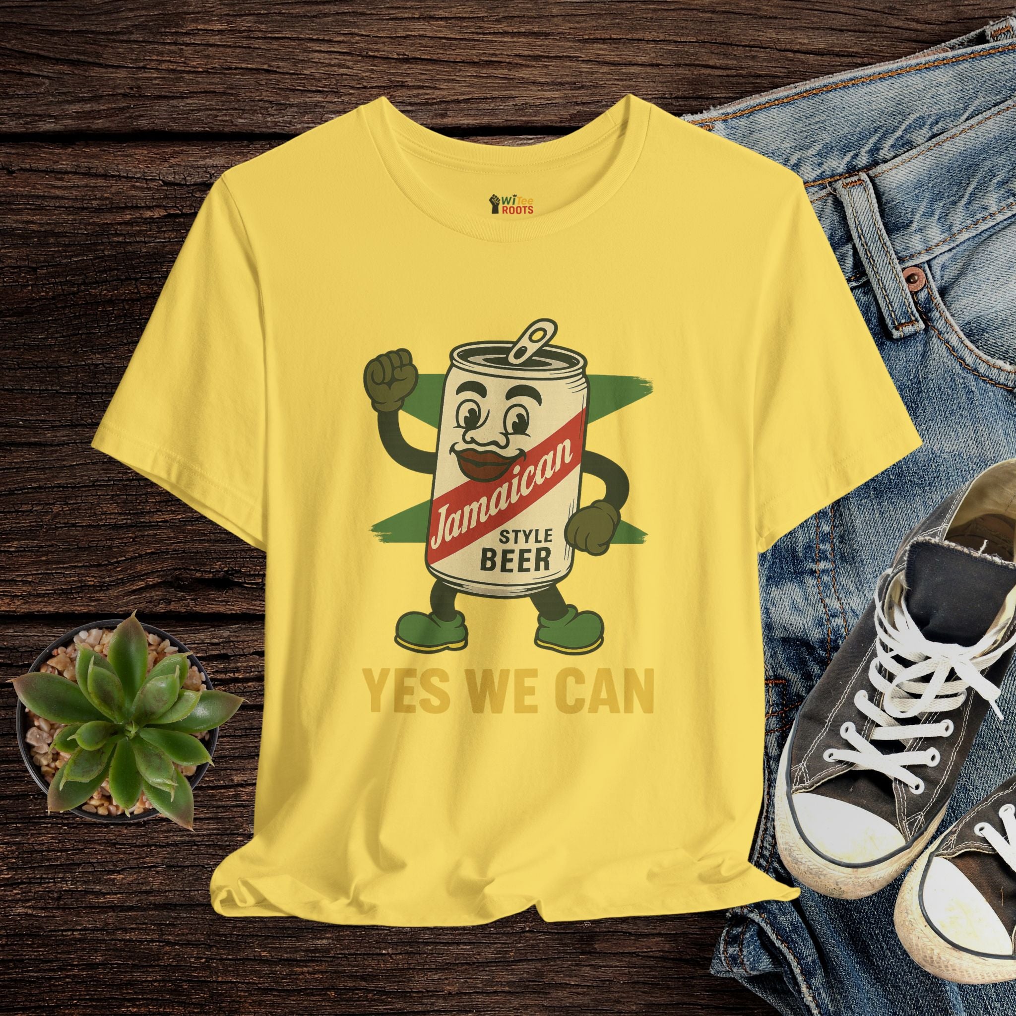 Yellow t-shirt with a cartoon beer can design and text, displayed on a wooden surface with jeans and sneakers.