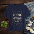 Navy blue t-shirt with 'RESIST' text on a wooden surface with jeans and sneakers.