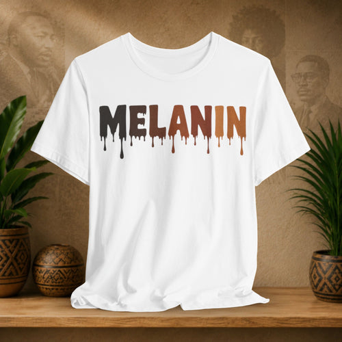 A white short-sleeve crewneck t-shirt with the word 'MELANIN' printed across the chest in a dripping paint style, transitioning from black to brown. The shirt is displayed on a wooden shelf flanked by potted green plants against a textured brown background with faint portraits.