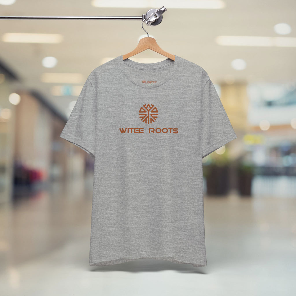 Gray t-shirt with 'Witee Roots' logo on a hanger in a blurred indoor setting