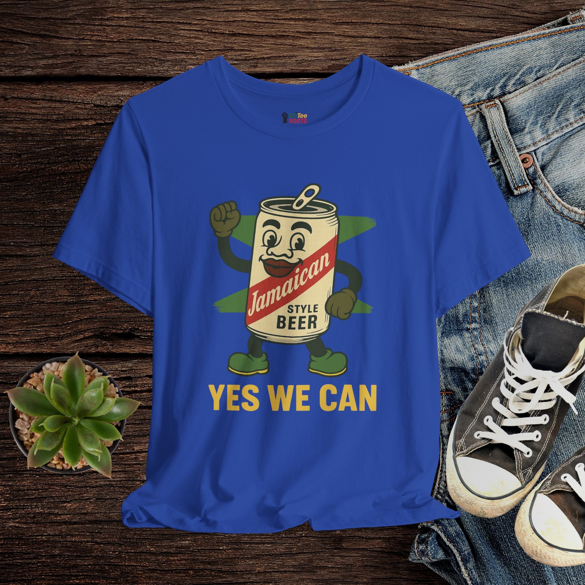 Blue t-shirt with Jamaican beer can graphic and 'Yes We Can' text on a wooden surface with jeans and sneakers.