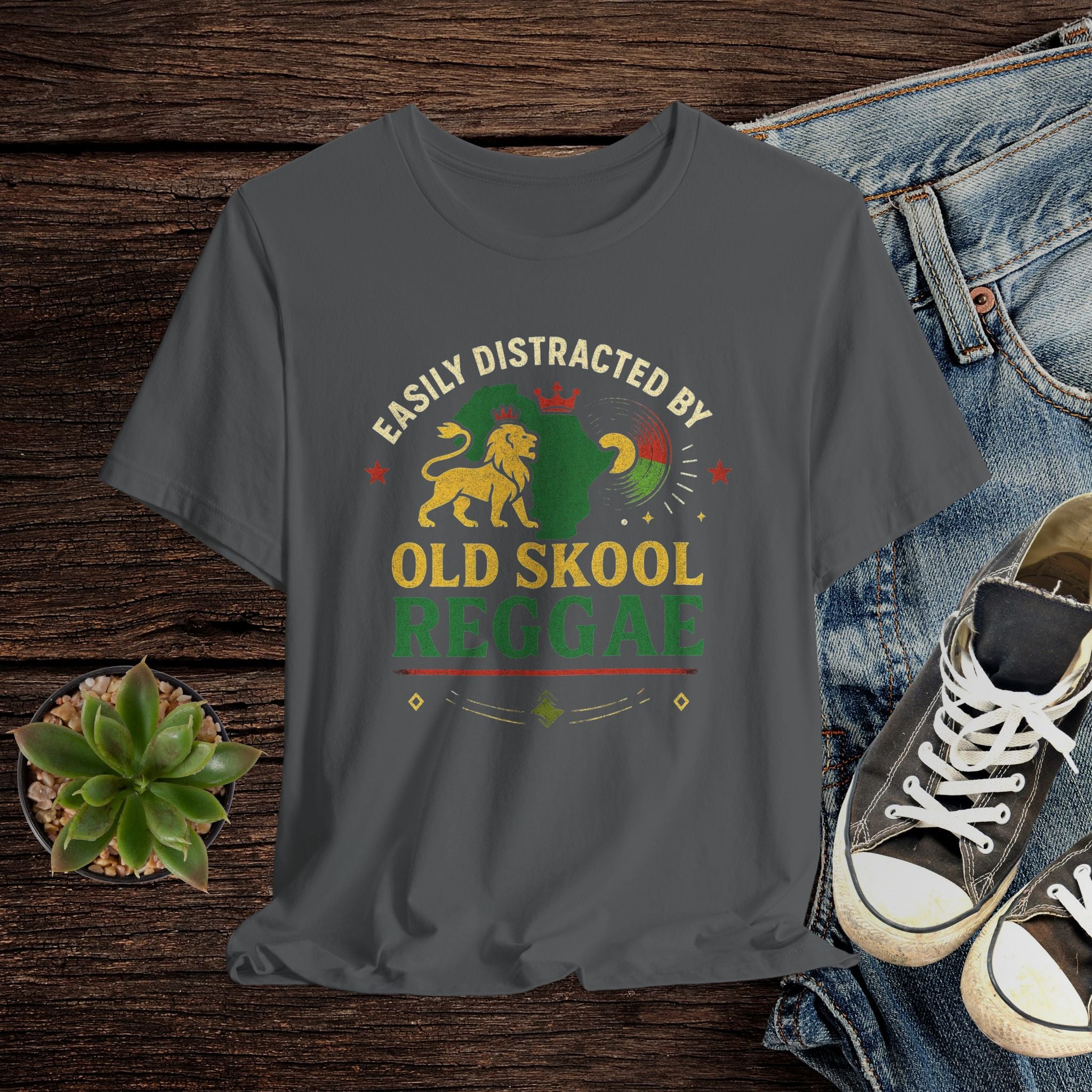 Gray t-shirt with 'Old Skool Reggae' design on a wooden surface with jeans and sneakers.