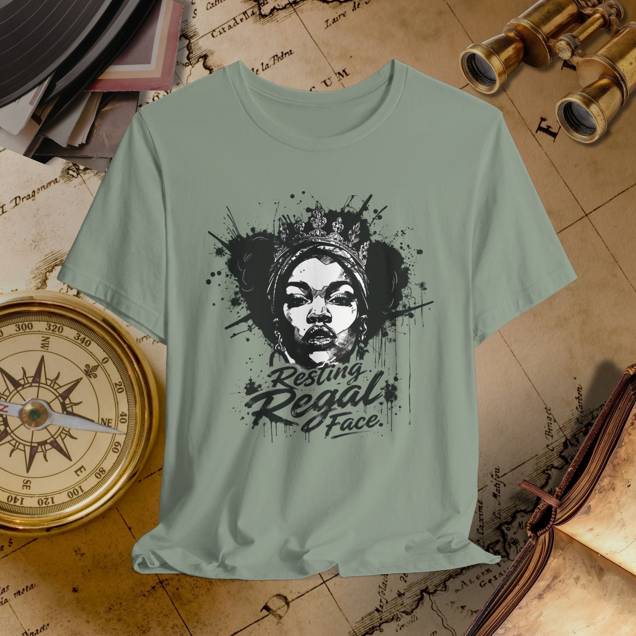 Light green t-shirt with a graphic design of a face and text 'Resting Regal Face' on a vintage map background.