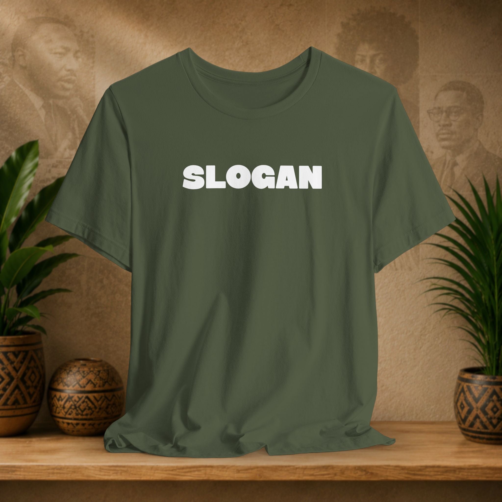 An olive green short-sleeve t-shirt with the word 'SLOGAN' printed in bold white capital letters across the chest, displayed on a wooden shelf with decorative plants and textured background.
